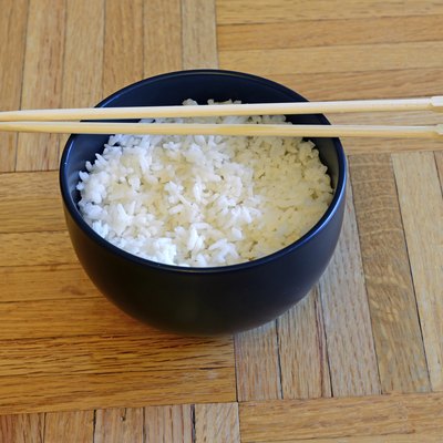 Bowl of white rice and chopsticks on wooden table