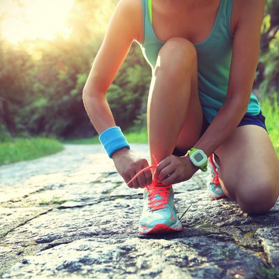 young woman runner tying shoelaces on stone trail
