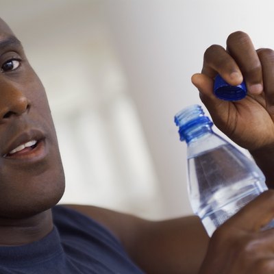 Bald man holding bottle of water with cap off, close-up, part of