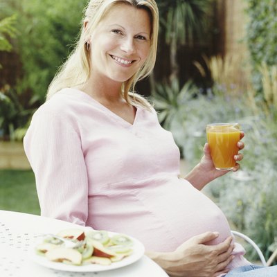 Portrait of a Pregnant Woman Sitting at a Garden Table Holding Her Stomach and Smiling