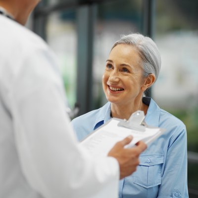 Close-up of doctor talking to mature patient while holding clipboard