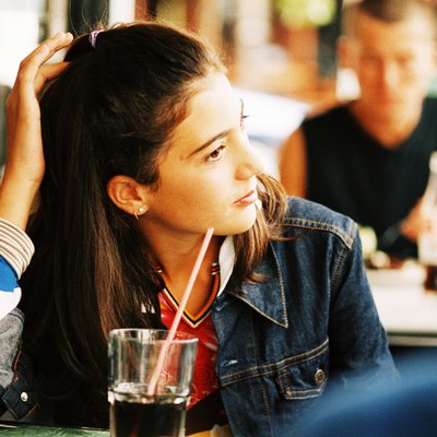 Teenage girl (14-16) sitting in a cafe with other people in the background