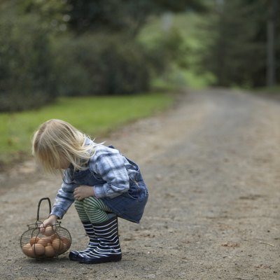 Young girl (3-4) squatting on road by basket with eggs, side view