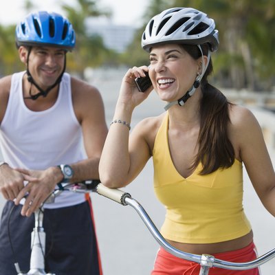 Hispanic woman on bicycle talking on cell phone while boyfriend waits
