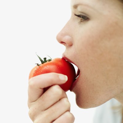 side profile of a young woman biting into a tomato