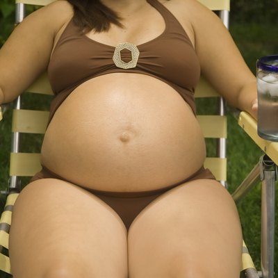 Pregnant woman laying in lawn chair wearing bathing suit