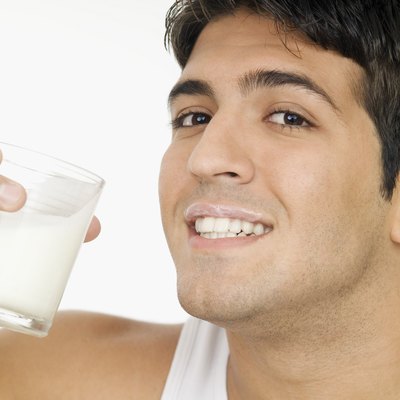Smiling young man with milk mustache and holding glass of milk, close-up