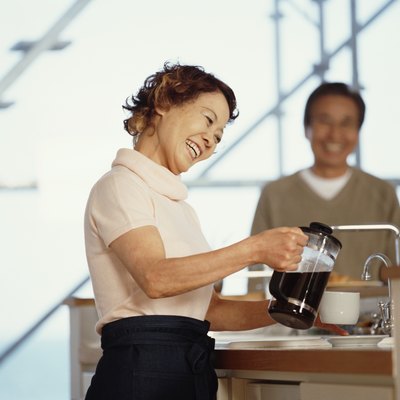 Senior woman pouring coffee in kitchen, senior man standing in background