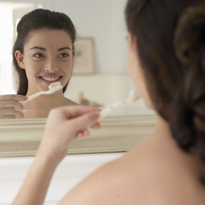 Young woman holding toothbrush, smiling, reflection in mirror