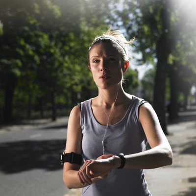 Young woman jogging on street with mp3 player, checking time