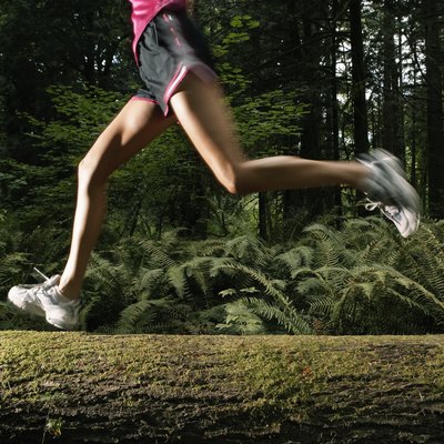 Woman running on log in forest, low section (blurred motion)