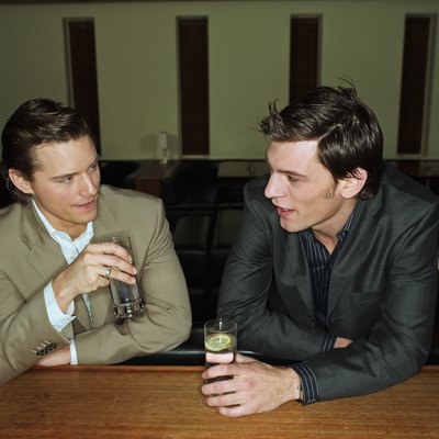 Two young men having drinks leaning on bar