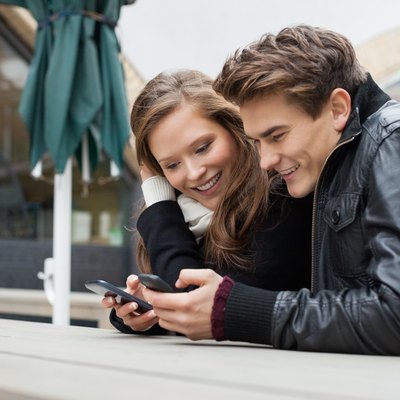 Couple Using Mobile Phone While Leaning On Bench