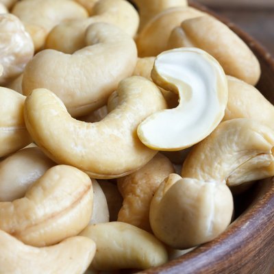 Wooden bowl of cashew nuts from above. On dark wood.
