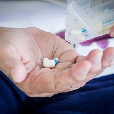 old woman hand pouring pills from a pill reminder box