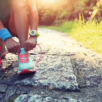 young woman runner tying shoelaces on stone trail
