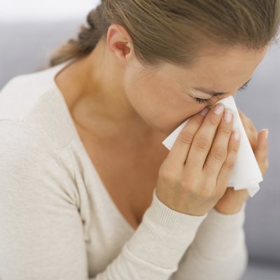young woman sitting on couch and blowing nose