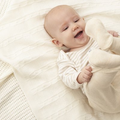 Baby girl (3-6 months) lying on blanket, smiling