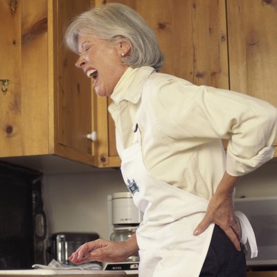Woman standing in a kitchen holding her back in pain