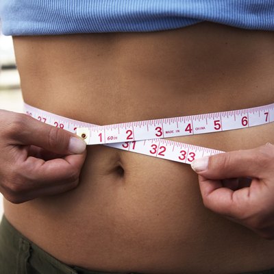 Mid section view of a woman measuring her waist with a tape measure