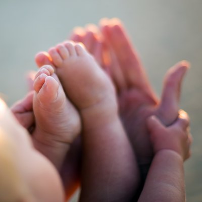 Little baby feet on mothers hands outdoors at backligh