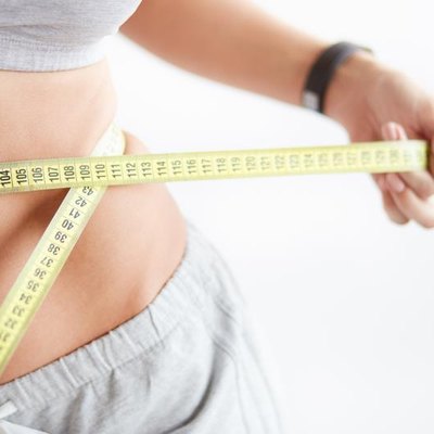 Bright closeup of slim young woman measuring her thin waist with a tape measure on white background