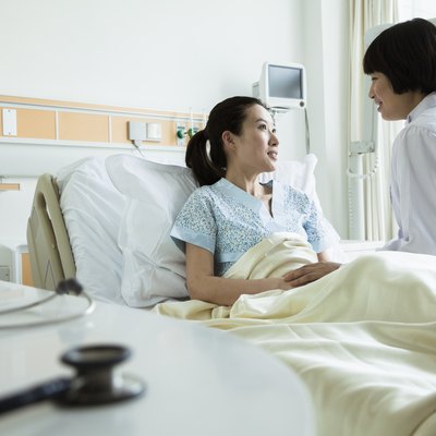 Female doctor sitting on hospital bed and discussing with young female patient