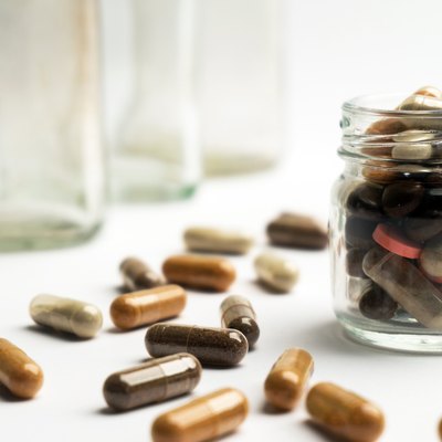 Different pills and capsules in glass jar on white background.