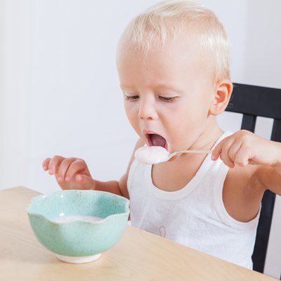 Little cute child boy eating yogurt himself, morning breakfast