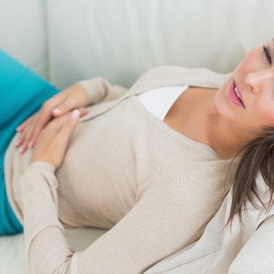 Sick woman lying on sofa with stomach ache
