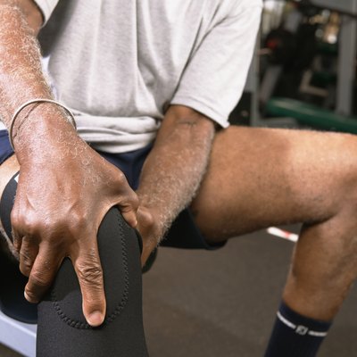 Senior man in gym wearing knee strap, holding knee, close-up