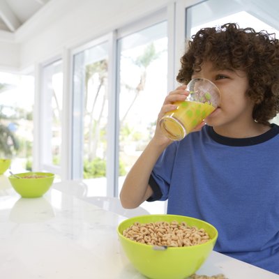 Boy (8-10) at table, drinking orange juice