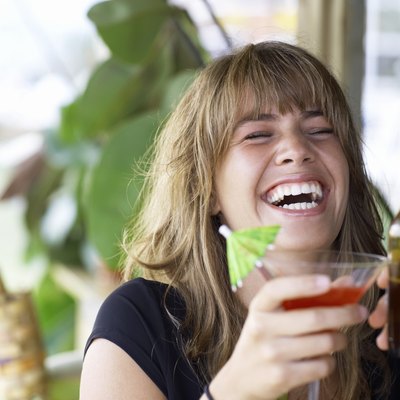 Young woman toasting drink with friend, laughing, close-up