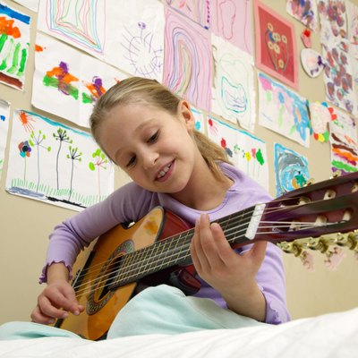 Girl (5-7) playing acoustic guitar on bed, low angle view