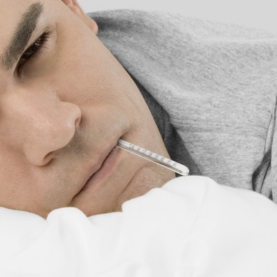 Mid adult man in bed with thermometer in mouth