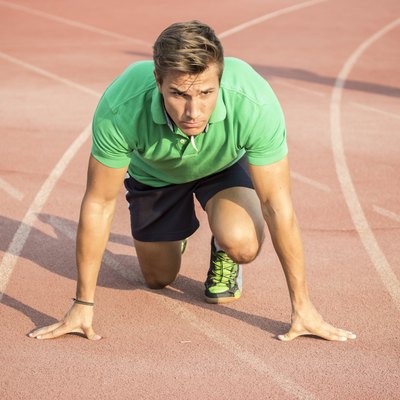 Male sprinter in clothes at start position, on red track.