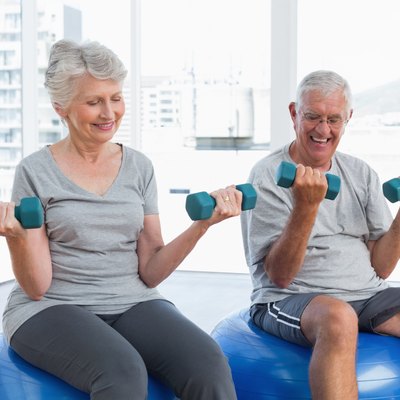 Happy senior couple sitting on fitness balls with dumbbells