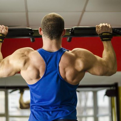 Professional bodybuilder with ideal muscular body doing pull-ups in the gym