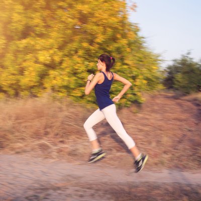 Young woman running on a rural road in autumn forest