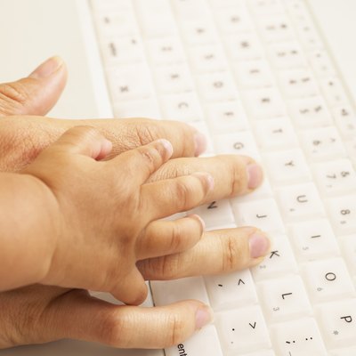 Close-up of a baby's hand holding an adult's hand on a laptop