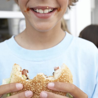 Boy (9-11) holding hamburger with 'bites' missing, smiling, close-up