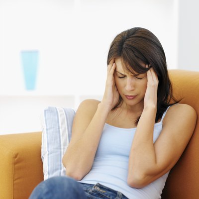 Close-up of young woman sitting on sofa with hand touching head