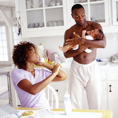 a young woman talking on the phone and a young man standing and holding a baby