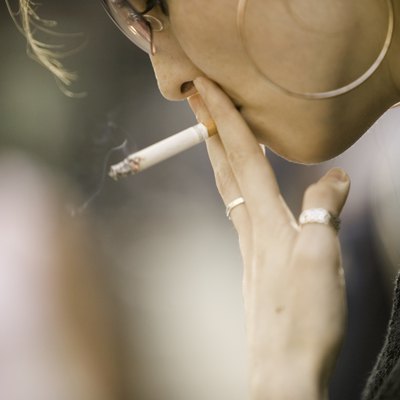 Young woman wearing sunglasses, smoking outdoors, close-up