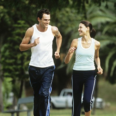 Mid adult man and woman jogging in park,looking in eyes and smiling