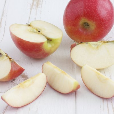 Pink lady apples cut on a white rustic wood table.
