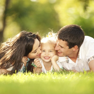 Happy mother and father kissing their daughter in the park