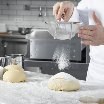 Chef sifting flour over a ball of dough