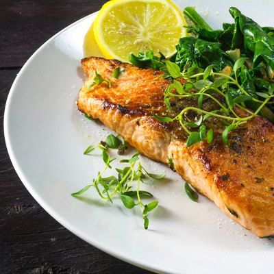 grilled salmon withspinach on a white plate, dark wooden table