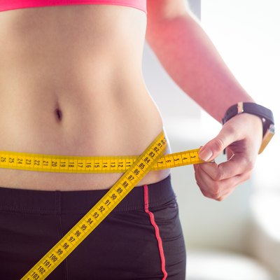 Slim woman measuring waist with tape measure